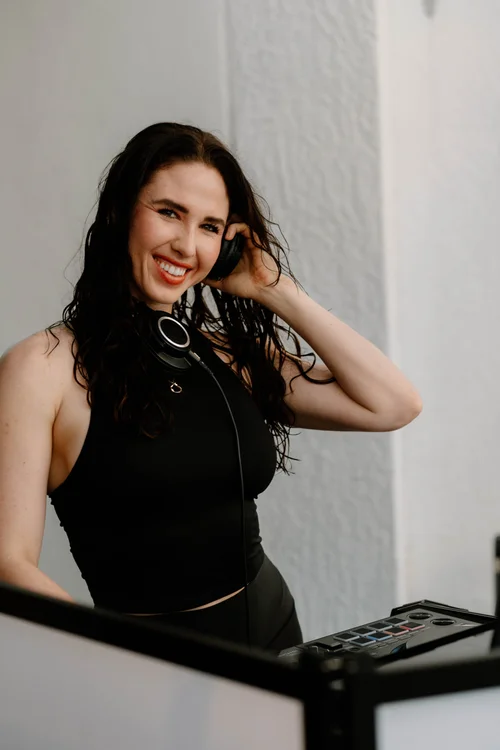 DJ Alejandra smiling with headphones at her DJ equipment