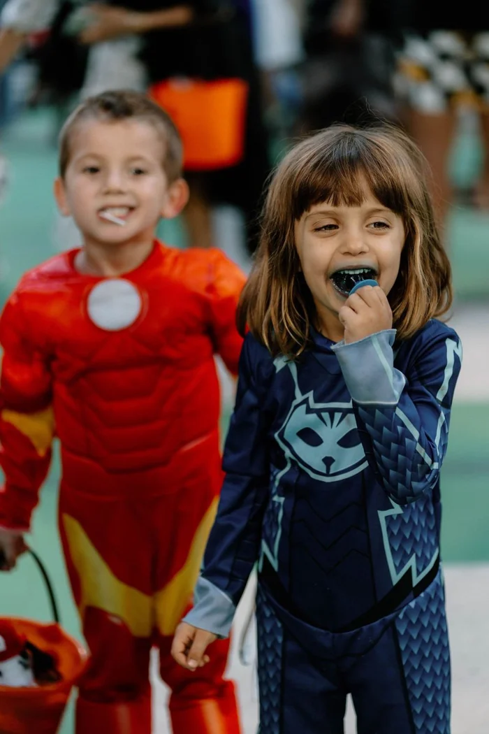 Two children wearing red and blue superhero costumes enjoy treats together